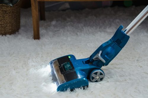 pexels-photo-9462316-9462316 Modern blue vacuum cleaner on a white fur carpet in a cozy indoor setting.